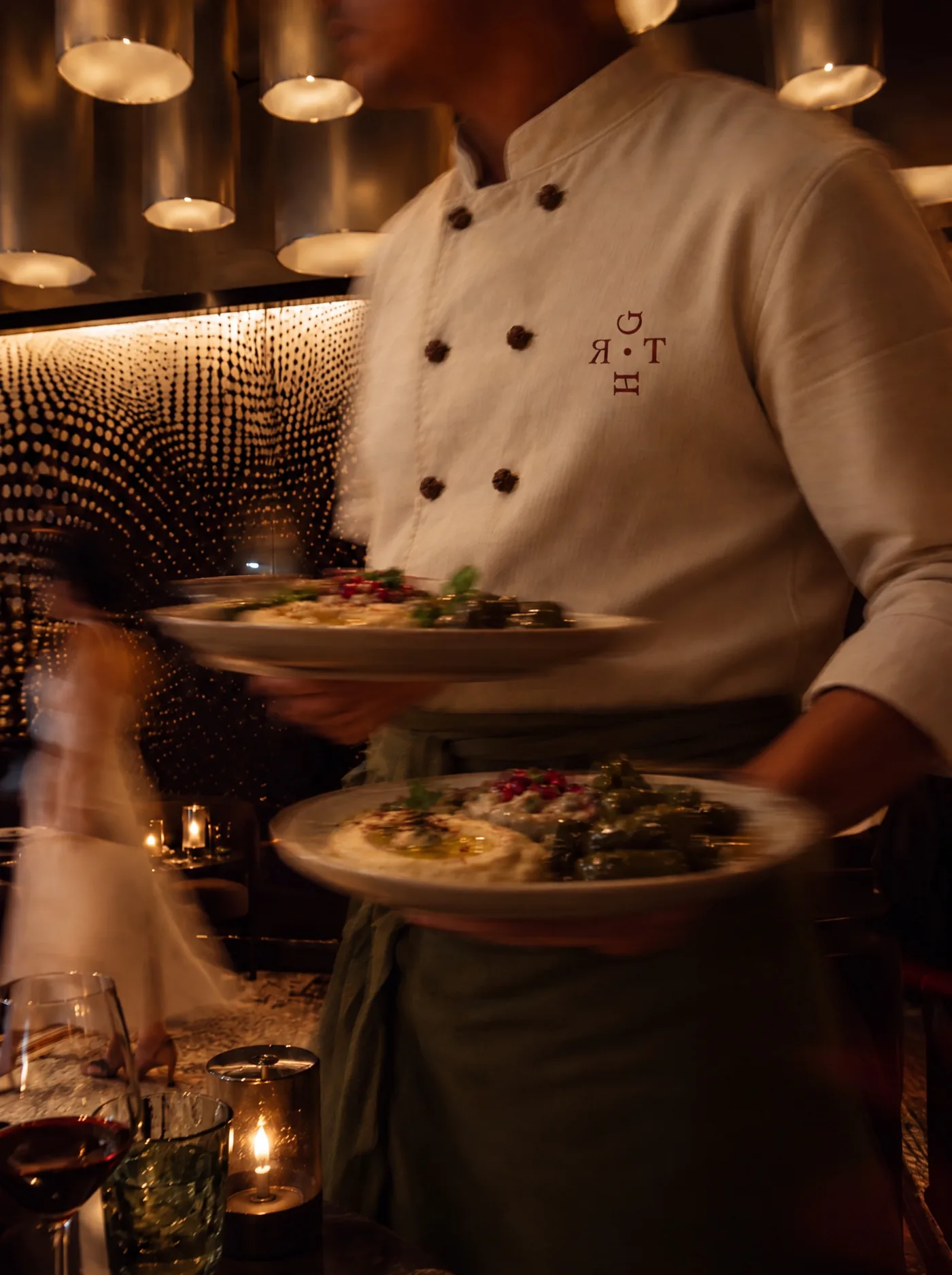 Chef in a cream jacket with the wine icon, carrying mezze